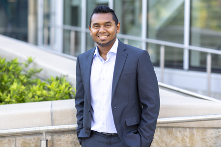 Shehan it button up shirt and navy blue suit standing outside
