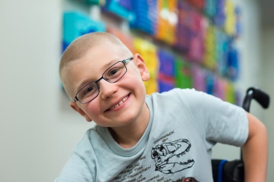 patient alex on campus hallway smiling with glasses on – in wheel chair
