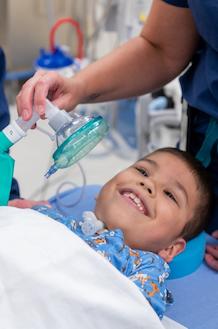 male child patient laying down in blue hospital gown smiling.